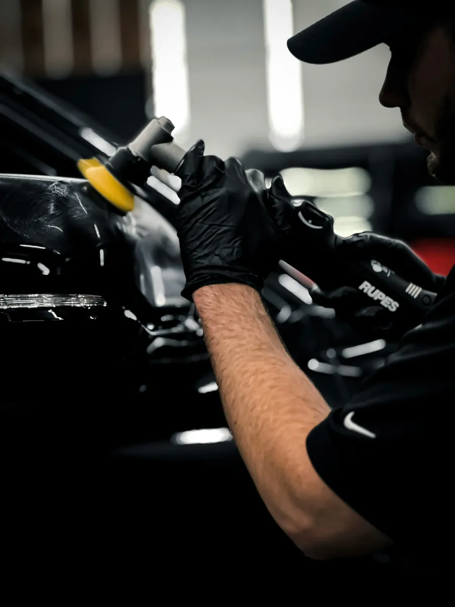 A technician running a polisher over a black panel